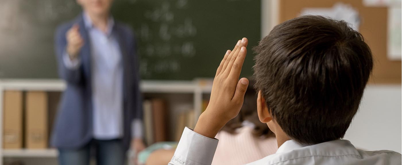 Little boy in classroom struggling to see tje teacher and chalk board